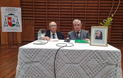 Luis Armando Galeano y Rafael Montiel sentados tras una mesa, ambos en traje, en un ambiente formal con decoración religiosa.