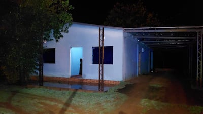 Ambiente exterior nocturno de una vivienda azul, con una figura oscura sugerente de actividad dentro.