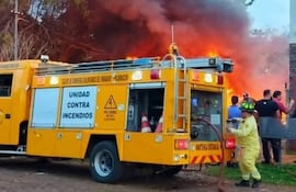 Bombero vestido con uniforme amarillo opera una manguera mientras testigos observan el incendio de cubiertas, generando humo negro.