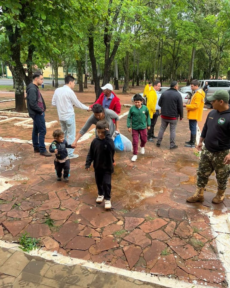 Grupo de niños y adultos en un parque, conversando. Un hombre de camisa blanca estrecha la mano de otro con abrigo rojo.