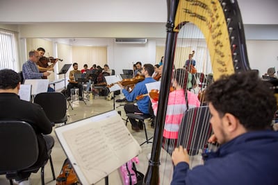 Músicos de la Orquesta Sinfónica del Congreso Nacional ensayan, con director mayor de gafas al frente y varios instrumentos visibles.