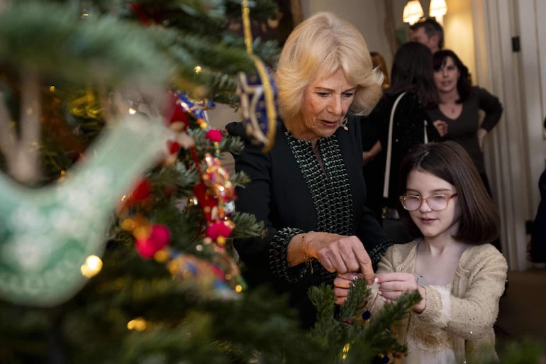 La reina Camilla y la pequeña Myla decorando el árbol navideño de Clarence House. (Aaron Chown / POOL / AFP)