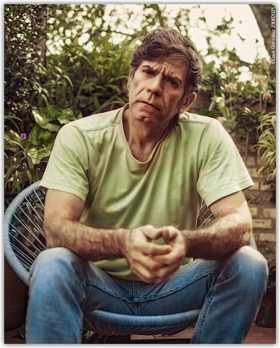 Héctor Micó con camiseta verde claro y jeans sentado en una silla moderna, rodeado de plantas con expresión reflexiva.