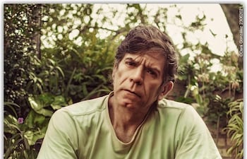 Héctor Micó con camiseta verde claro y jeans sentado en una silla moderna, rodeado de plantas con expresión reflexiva.