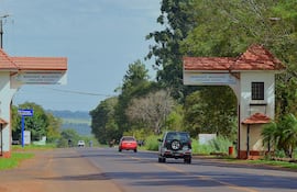Carretera hacia Bella Vista flanqueada por vegetación, con arcos de entrada y vehículos transitando.