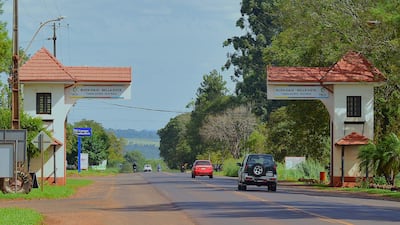 Carretera hacia Bella Vista flanqueada por vegetación, con arcos de entrada y vehículos transitando.