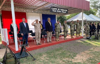 Seis personas en uniforme militar y trajes formales, en un acto solemne con fondo de bandera paraguaya.