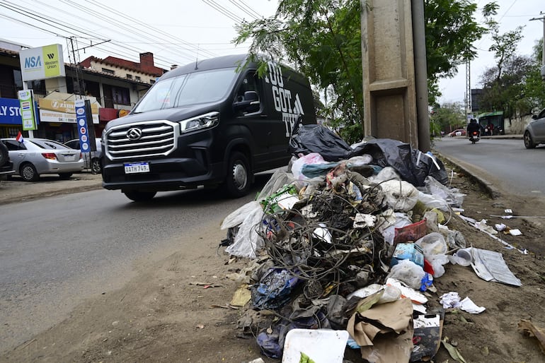 Acumulación de basura y un vehículo negro en la Avenida Artigas, con comercios borrosos detrás.