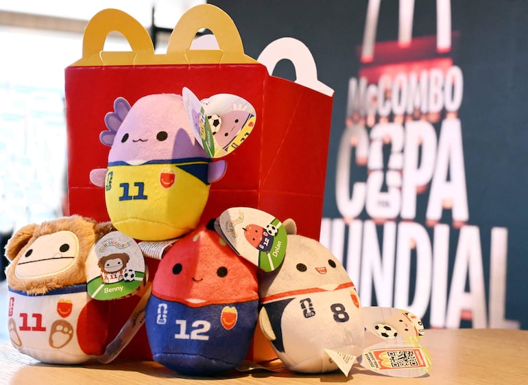 Cuatro peluches de fútbol en camisetas numeradas, dispuestos sobre una caja roja promocional de comida rápida.