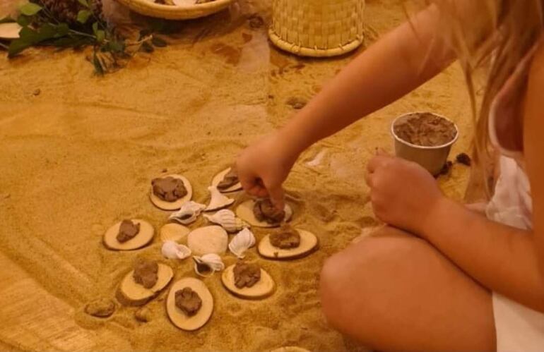 Niña sentada en el suelo, concentrada en su actividad creativa con conchas y madera en un ambiente natural.