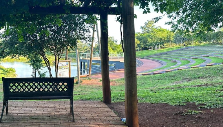 Banco de madera en el parque, con anfiteatro al fondo y vegetación rodeando el área tranquila.
