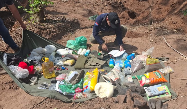 Dos personas revisan objetos en un lienzo verde en área forestal, rodeados de bolsas y documentación.