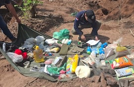Dos personas revisan objetos en un lienzo verde en área forestal, rodeados de bolsas y documentación.