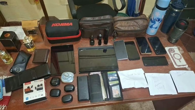 Mesa con varios teléfonos móviles, billeteras, perfumes y auriculares, en un ambiente interior organizado.
