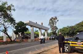 Varios obreros con cascos de seguridad laboran en la construcción del viaducto, mientras un vehículo policial observa la escena.