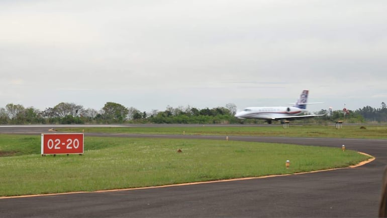 Un avión despegando en una pista nublada, con un cartel rojo que indica la pista '02-20' y vegetación al fondo.