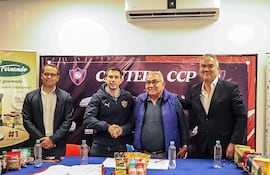 Cuatro hombres en mesa; uno en chaqueta negra, otro con chaleco azul y gafas, celebrando un acuerdo entre Cerro Porteño y Arco Iris.