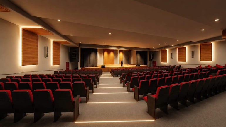 Una persona de pie en el escenario del auditorio vacío, con asientos negros y rojos en un espacio moderno y iluminado.