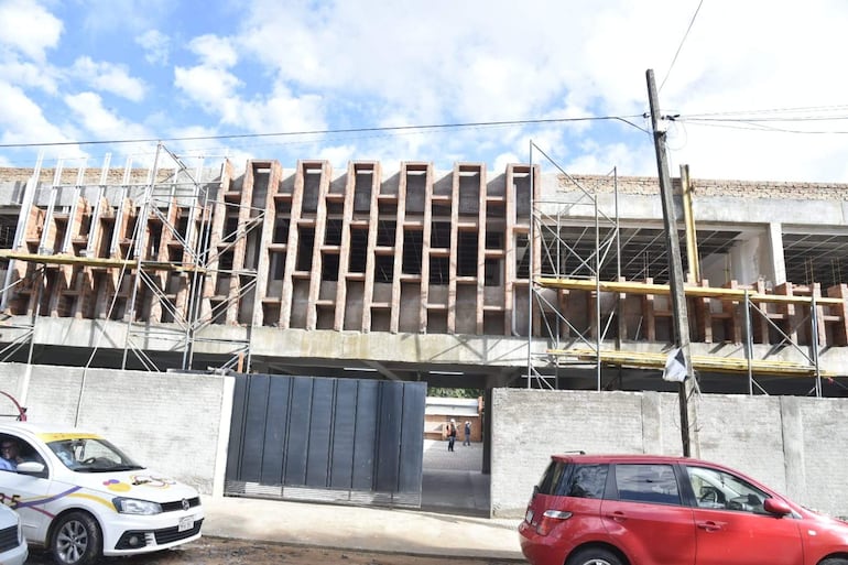 Construcción en progreso del Colegio Técnico Nacional, con andamiaje y dos vehículos estacionados en primer plano bajo cielo nublado.