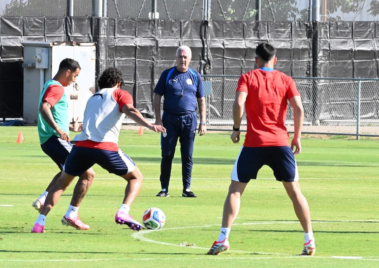 Gustavo Alfaro en chándal azul observa a Alejandro Romero Gamarra y otro jugador en camisetas de entrenamiento durante un ejercicio.