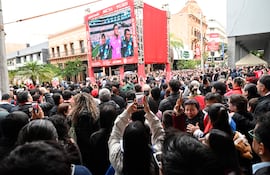 Multitud de hinchas con teléfonos móviles, mirando una pantalla gigante, vestidos con colores festivos de apoyo a Paraguay.