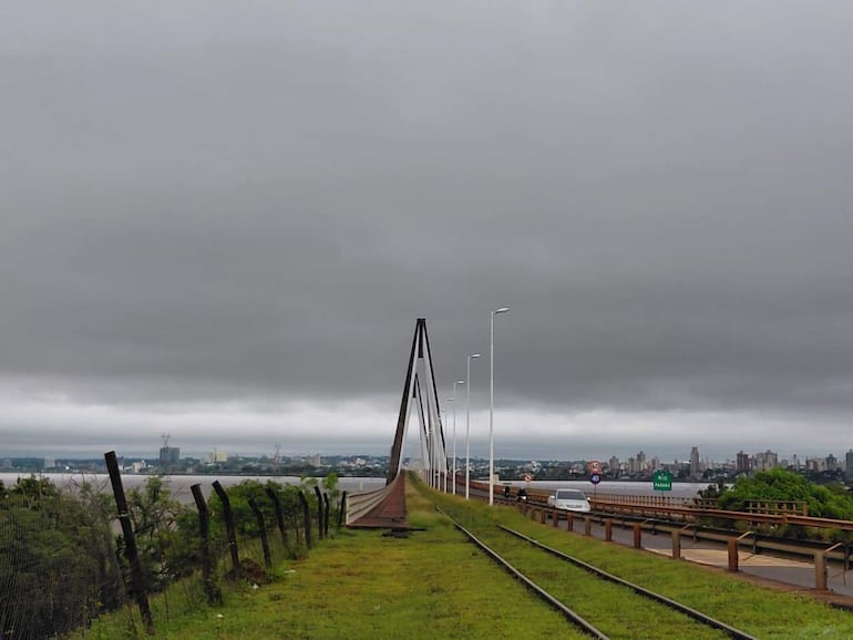 Carretera en día nublado con puente sobre el río Paraguay y vehículos, sin personas visibles.