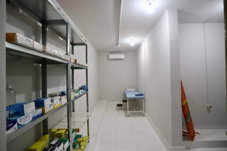 Ambiente limpio y bien iluminado con estantes metálicos y camilla en un cuarto de atención sanitaria.