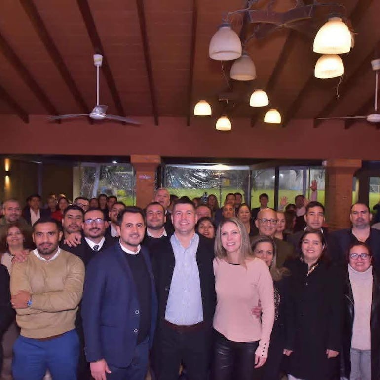 Emilio Acevedo rodeado de más de 40 abogados sonrientes en un ambiente festivo interior, con vestimenta variada.
