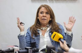 Celeste Amarilla con chaqueta de mezclilla y blusa blanca, sosteniéndose de un micrófono mientras levanta una mano con énfasis.