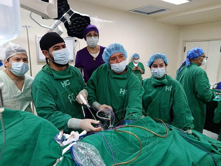 Equipo quirúrgico en el quirófano, con seis personas en ropa médica verde y un médico concentrado en la operación.