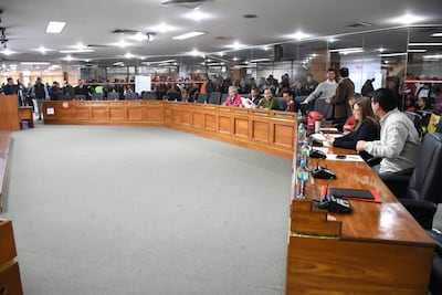 Miguel Sosa y Juan Carlos Ozorio Admen discuten en mesa, rodeados de funcionarios sentados y audiencia atenta en ambiente gubernamental.