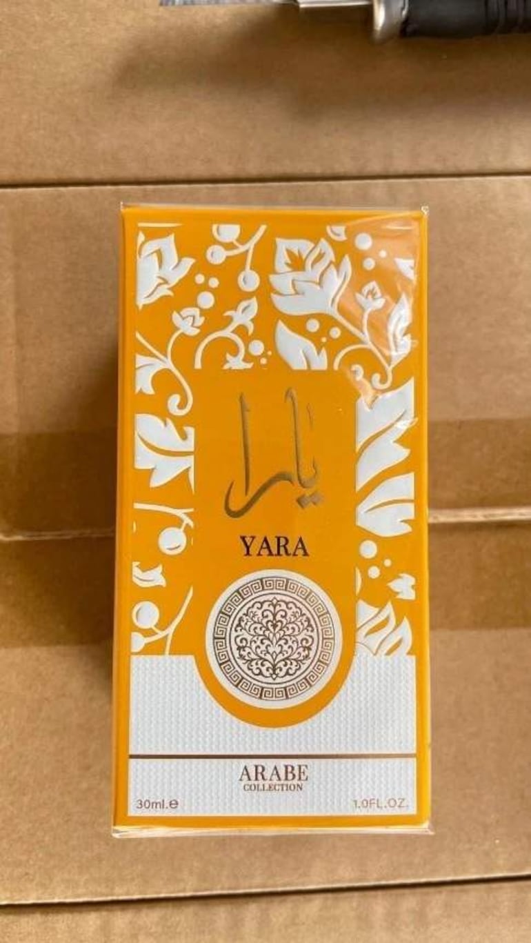 Caja de perfume amarilla con el nombre 'YARA', patrón floral, en un fondo de cartón marrón.
