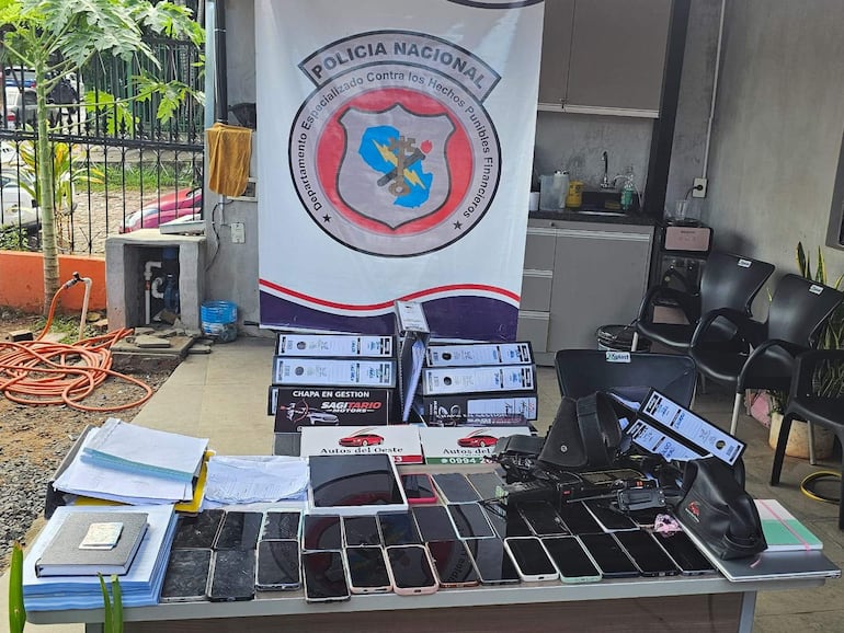 Ambiente de la Policía Nacional con documentos, celulares y pistola sobre una mesa, sin personas visibles.