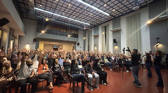 Médicos votan en asamblea cuestionando aumento salarial propuesto por el gobierno en un salón amplio.