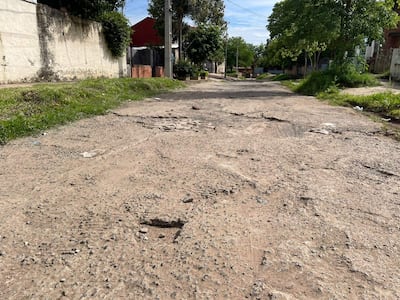 Calle deteriorada en Itay, sin personas, con baches y cercas claras a los lados.