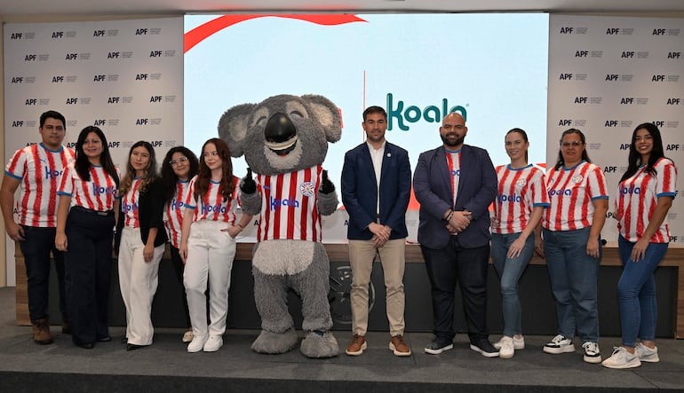 Mujer con vestimenta de selección paraguaya y hombre con chaqueta azul en evento formal de Koala y la APF, con logo de Albirroja visible.