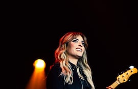 Kany García sonríe mientras sostiene un micrófono, luciendo elegante en el escenario rodeada de luces y músicos.