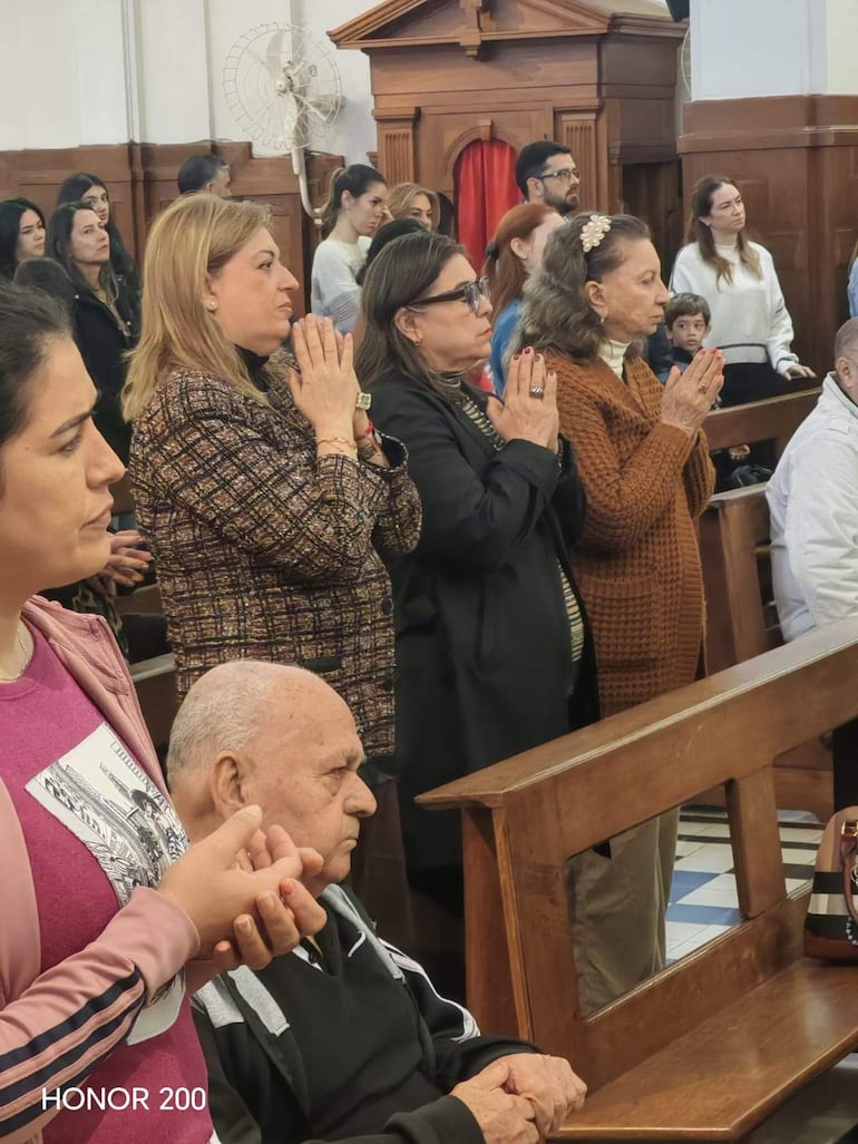 Sandra Quiñonez en el centro, rodeada de personas en oración, en un ambiente solemne con mobiliario de madera.