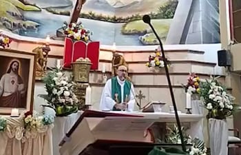 Sacerdote Patricio Alfredo Sánchez Molinari en altar con vestimenta litúrgica verde, crucifijo y decoración floral en un ambiente de culto.