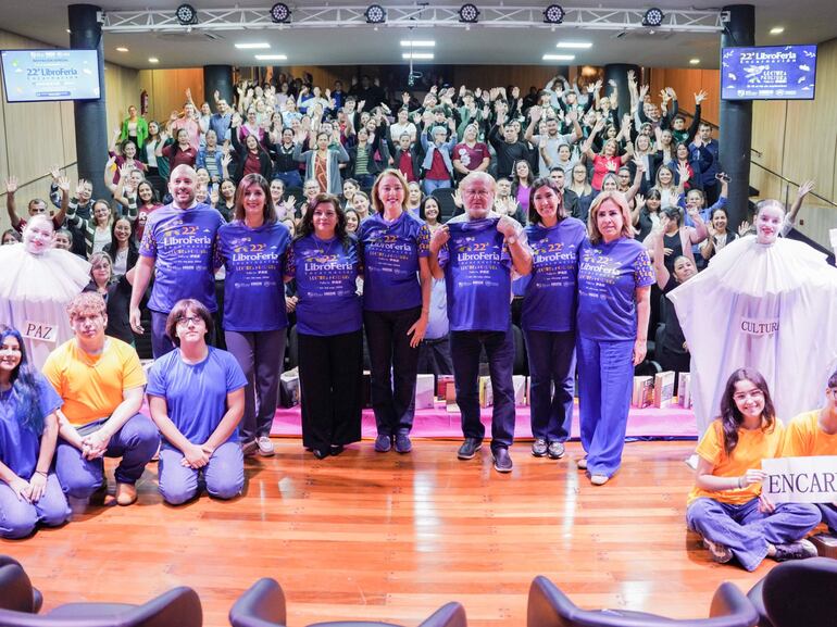 Grupo de personas con camisetas azules de la 22ª Libroferia, celebrando en un auditorio. Ambiente festivo y colorido.