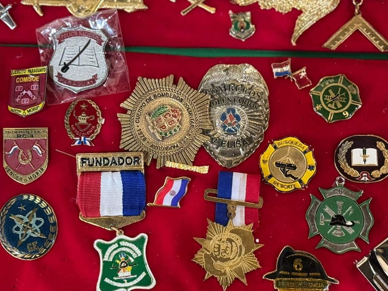 Colección de insignias y medallas sobre fondo rojo, destacando una medalla con los colores de la bandera paraguaya.