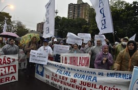 Mujeres y hombres con capas de lluvia sostienen pancartas en una manifestación, destacando un cartel que dice 'Primer empleo para profesionales desempleados'.