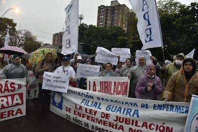 Mujeres y hombres con capas de lluvia sostienen pancartas en una manifestación, destacando un cartel que dice 'Primer empleo para profesionales desempleados'.
