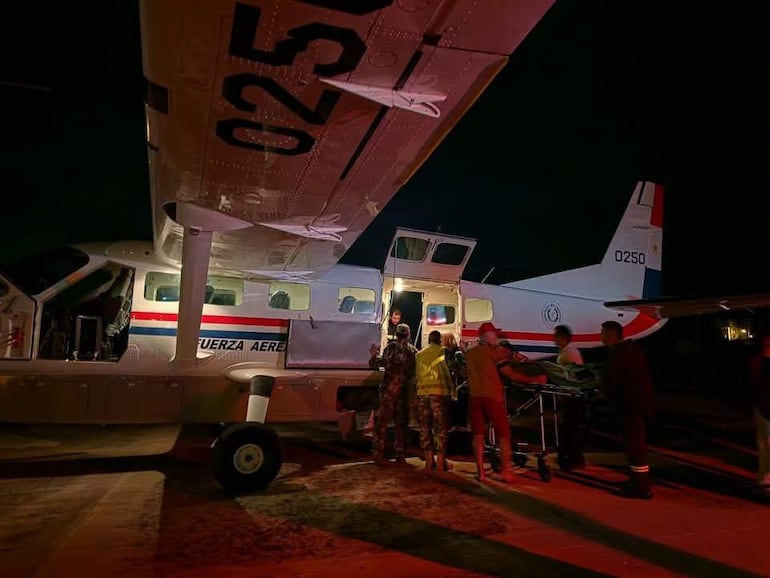 Grupo de personas en uniforme militar y paramédicos cargan una camilla hacia un avión de la Fuerza Aérea, con luces encendidas en la entrada.