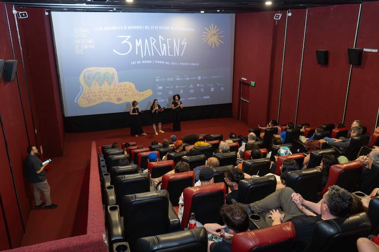 Tres mujeres de pie en un cine, una leyendo un documento, en un ambiente moderno y oscuro durante el festival.