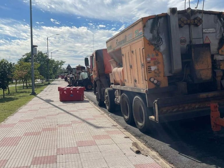 Varios camiones de construcción estacionados a lo largo de la acera en una calle urbanizada con césped y postes de iluminación.