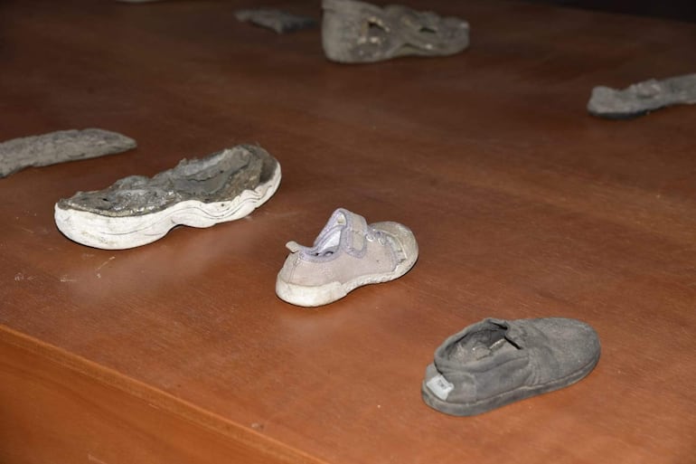 Tres pares de zapatos en mal estado sobre una superficie de madera, evocando la memoria de una tragedia en un acto conmemorativo.