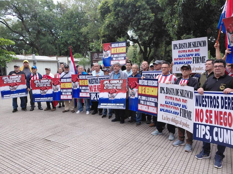 Grupo de hombres con camisetas de Olimpia y pancartas en la Plaza de la Justicia, manifestándose en un ambiente tranquilo.
