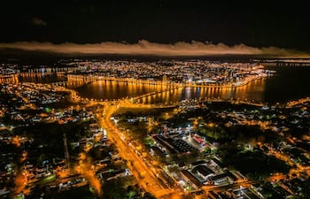 Vista aérea de Encarnación iluminada por luces urbanas, con calles y un río reflejando su brillo nocturno.