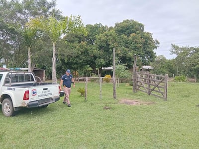 Hombre en uniforme azul de criminalística camina hacia la cámara, acompañado de un vehículo Isuzu con la palabra 'CRIMINALISTICA' en el costado.